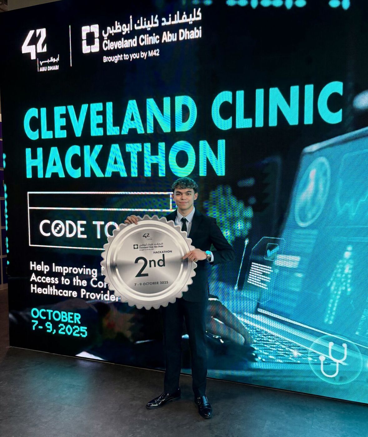 Ismail holding the 2nd place award in front of the Cleveland Clinic Hackathon LED wall